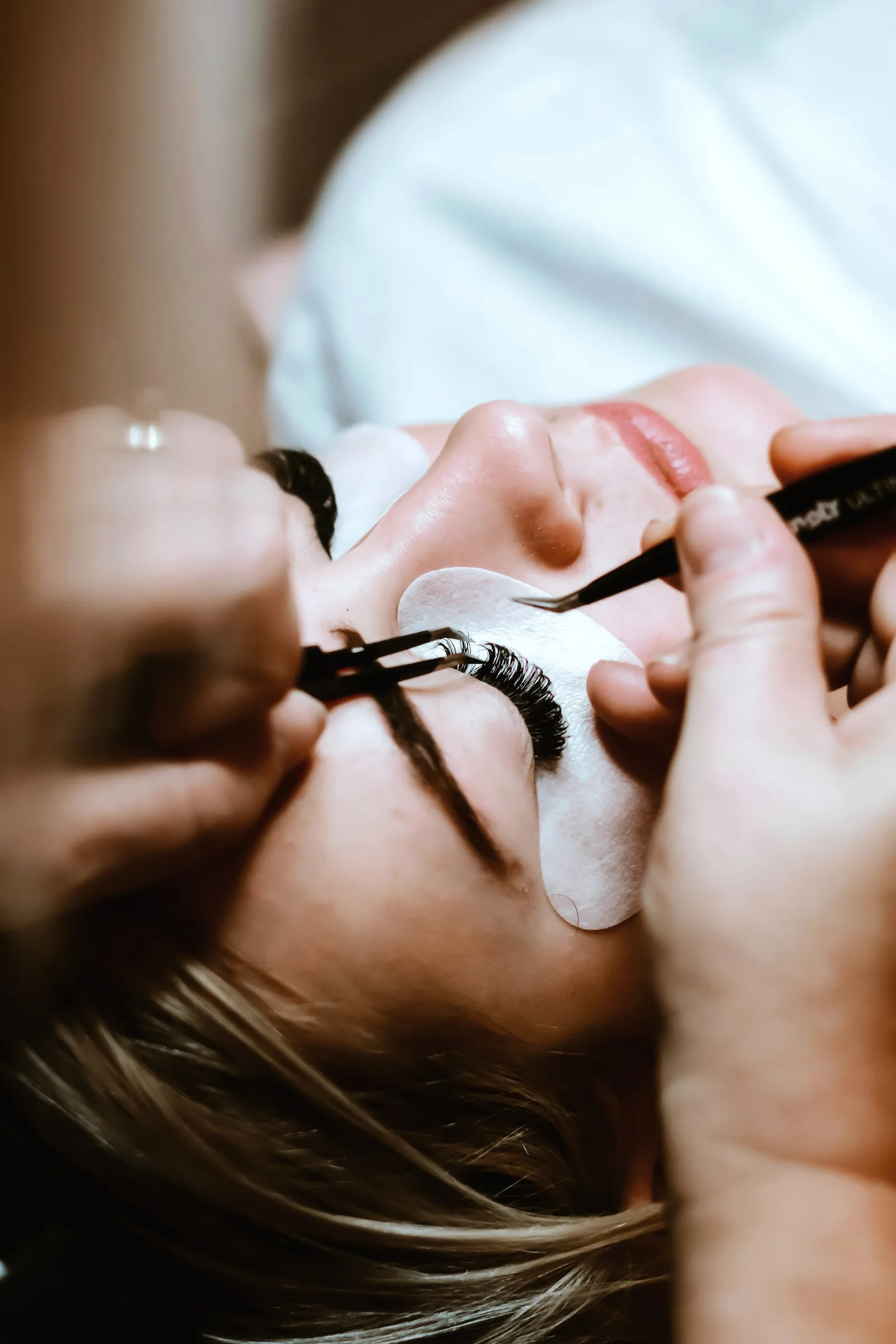 Pose d'extensions de cils à la pince, geste précis en institut