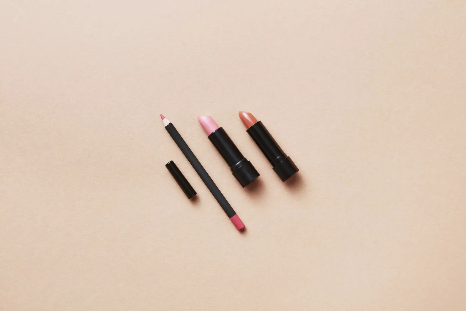 Rouges à lèvres nude et crayon posés sur un fond beige rosé